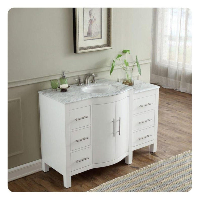 White bathroom vanity with marble top, curved design, drawers, and houseplant by sheer curtained window
