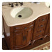 Curved wooden bathroom vanity with cream countertop, oval sink, and decorative cabinet hardware in rich brown wood tone.