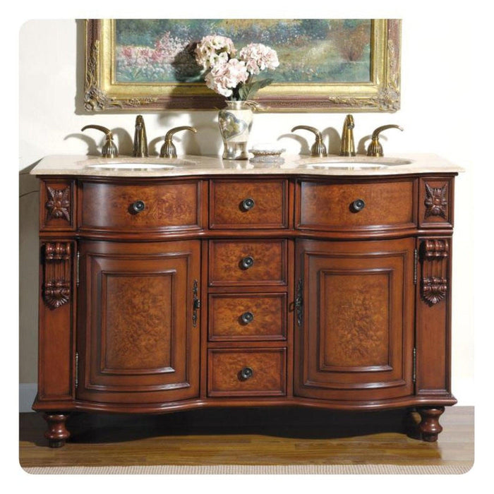 Ornate wooden bathroom vanity with curved drawers, marble top, double sinks, and decorative carved details, topped with pink hydrangeas and framed artwork.