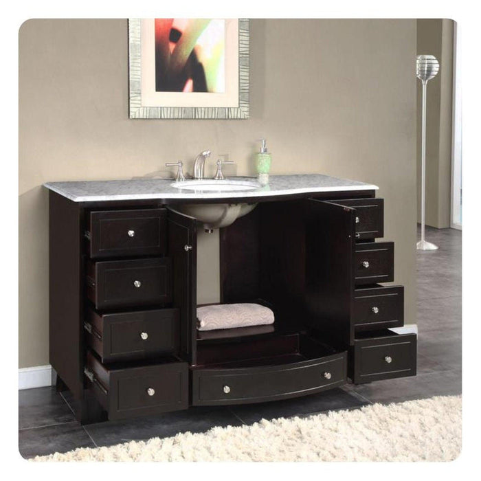 Dark wood bathroom vanity with marble top, multiple drawers, central sink, and white fluffy rug underneath.