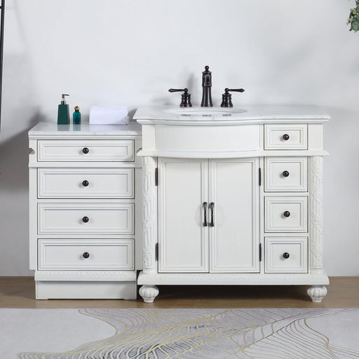 White bathroom vanity with marble top, black fixtures, four drawers, and central cabinet, styled with green soap dispensers and white towel.