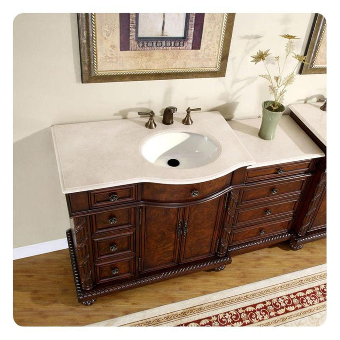 Elegant wooden bathroom vanity with white marble top, ornate dark wood cabinetry, bronze faucet, and small vase of delicate flowers.