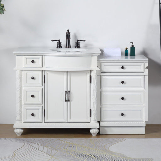 White bathroom vanity with black fixtures, featuring double cabinets, multiple drawers, and a marble-style countertop with decorative bottles and folded towel.
