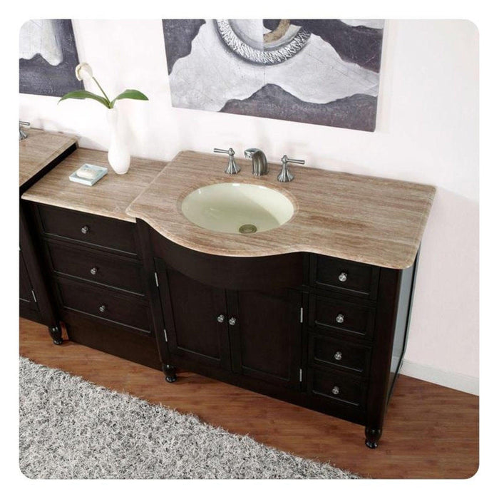 Dark wood bathroom vanity with curved travertine countertop and oval undermount sink, featuring multiple drawers and a white vase with a single flower.
