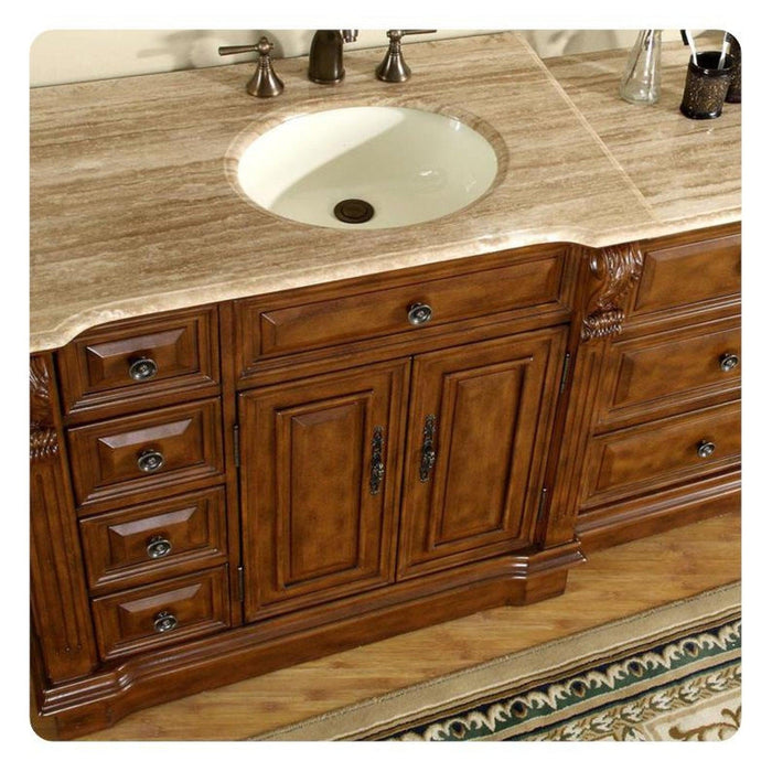 Rich wood bathroom vanity with marble countertop, white sink, and decorative metal faucet handles and drawer pulls.