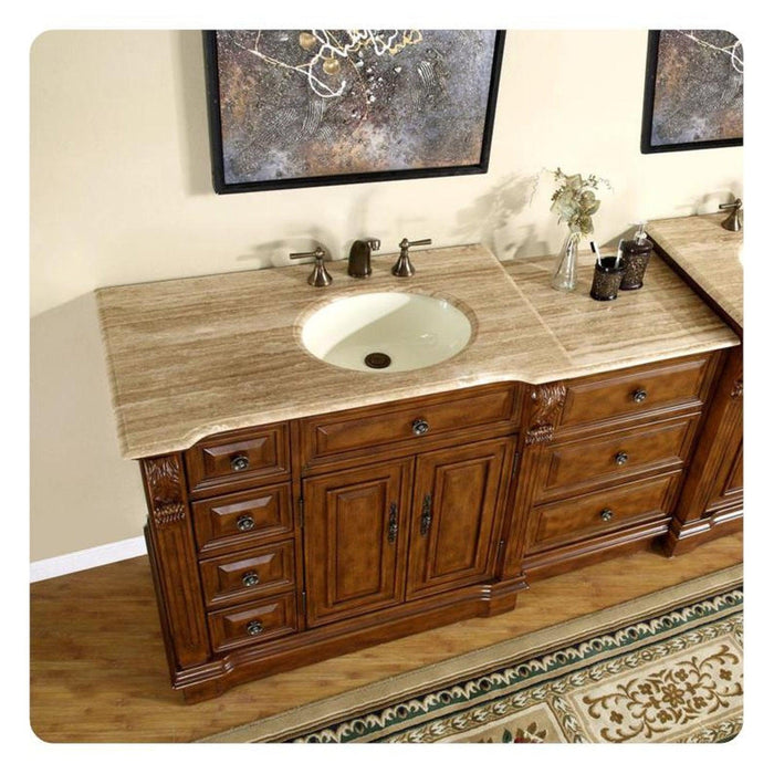 Rich wood bathroom vanity with travertine countertop, white sink, and decorative bronze fixtures, flanked by ornate artwork.