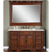 Rich wood bathroom vanity with white marble top, matching framed mirror, and antique brass fixtures