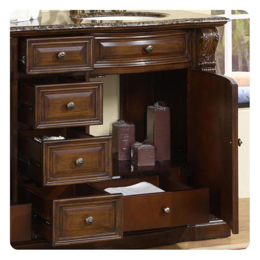 Dark wood bathroom vanity with marble top, multiple drawers, and burgundy candles displayed in open cabinet section.