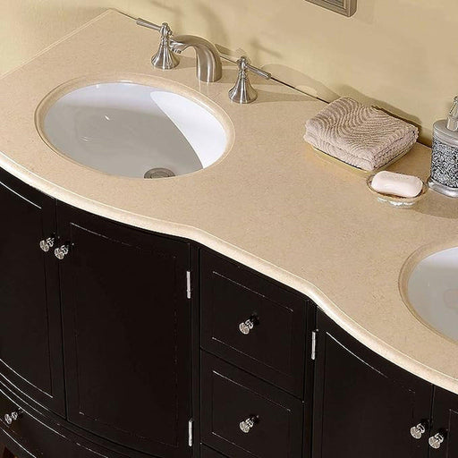 Curved black bathroom vanity with beige stone countertop, double white sinks, brushed nickel faucets, and a folded towel beside soap.