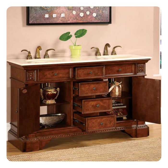 Rich wood bathroom vanity with white marble top, brass faucets, open drawers, and green plant in yellow pot