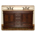 Rich wood double-sink bathroom vanity with marble top, ornate drawer pulls, and cabinet doors, mounted on tiled floor.