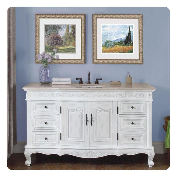 White vintage-style bathroom vanity with ornate details, framed landscape art, and a purple flower vase on light blue wall.
