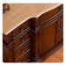 Ornate wooden dresser with curved drawers, detailed carved edges, and polished brass hardware on a light stone surface.