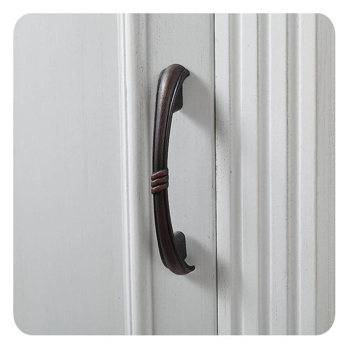 Weathered bronze door handle mounted on white vertical paneled surface, curved with subtle decorative wrapping detail