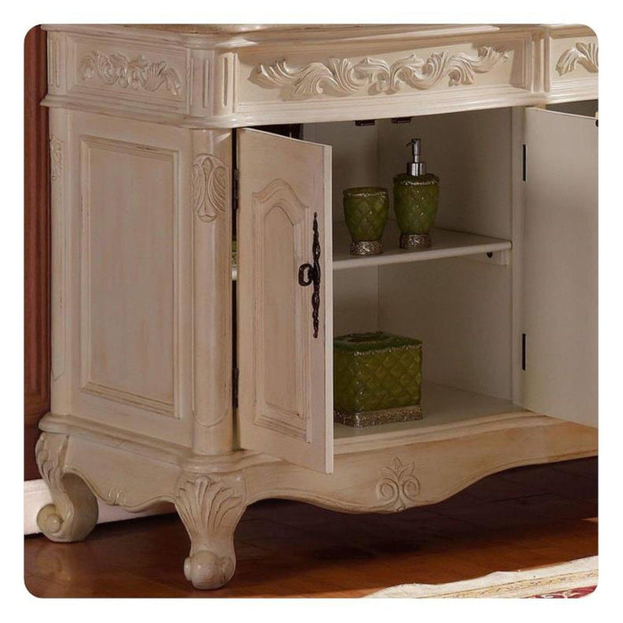 Antique white bathroom vanity with ornate carved details, curved legs, and open cabinet door revealing green ceramic accessories on shelves.