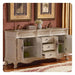 Ornate white bathroom vanity with open doors, revealing green accessories, marble top, decorative faucets, and floral vase.