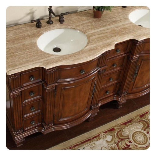 Ornate wooden bathroom vanity with curved drawers, white sink, and dark bronze faucet on travertine countertop.