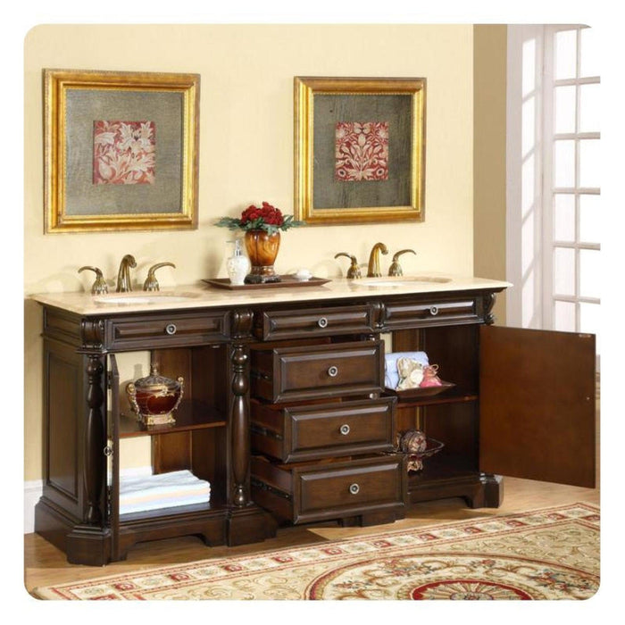 Dark wood bathroom vanity with marble top, double sinks, gold-framed art, red floral arrangement, and ornate area rug.