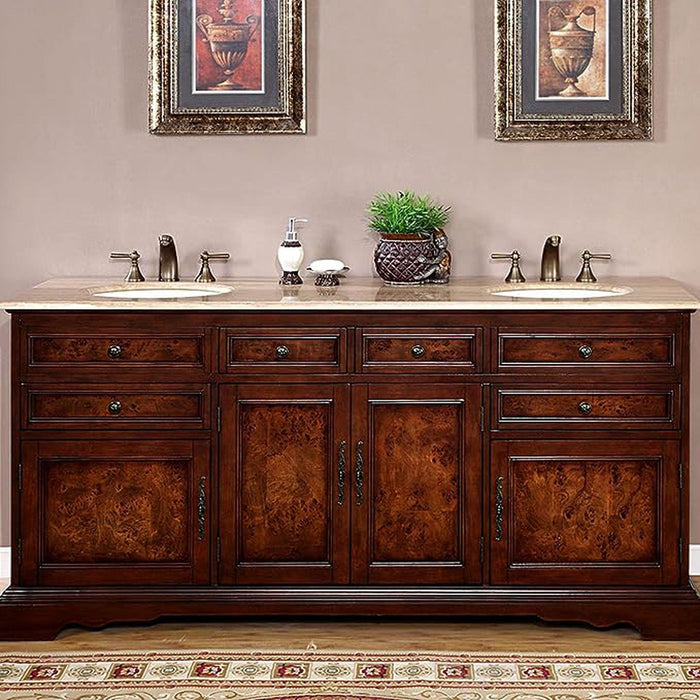 Rich wood double vanity with marble top, two sinks, and framed urn artwork above, accented by small plant and bathroom accessories.