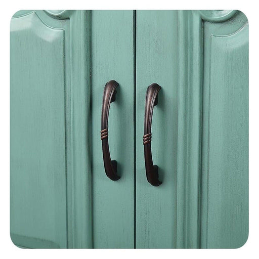 Two antique bronze door handles on a mint green wooden cabinet or closet, with vertical panels and curved decorative edges.