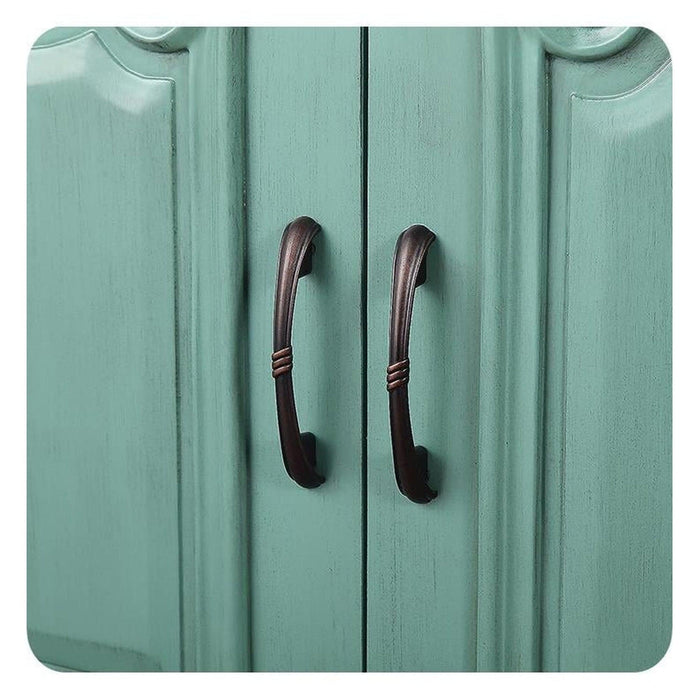 Two antique bronze door handles on a mint green wooden cabinet or closet, with vertical panels and curved decorative edges.