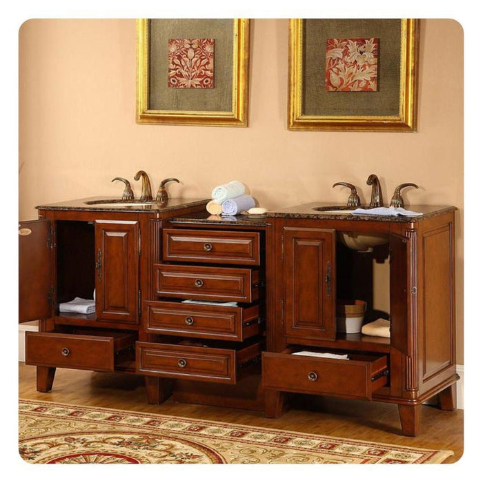 Rich wood bathroom vanity with marble top, multiple drawers open, ornate gold-framed artwork, rolled towels, and decorative area rug.