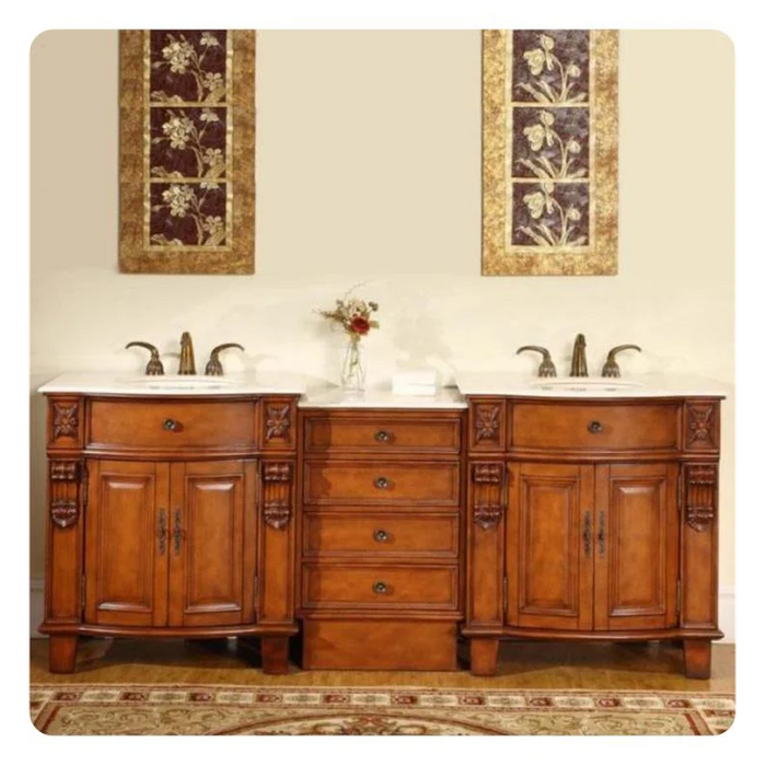Elegant wooden bathroom vanity with two sinks, ornate floral wall art, central drawers, and a small vase of flowers on white countertop.