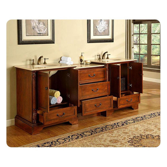Vintage wooden bathroom vanity with double sinks, marble countertop, open cabinet doors revealing towel storage and drawers, with framed art and window in background.