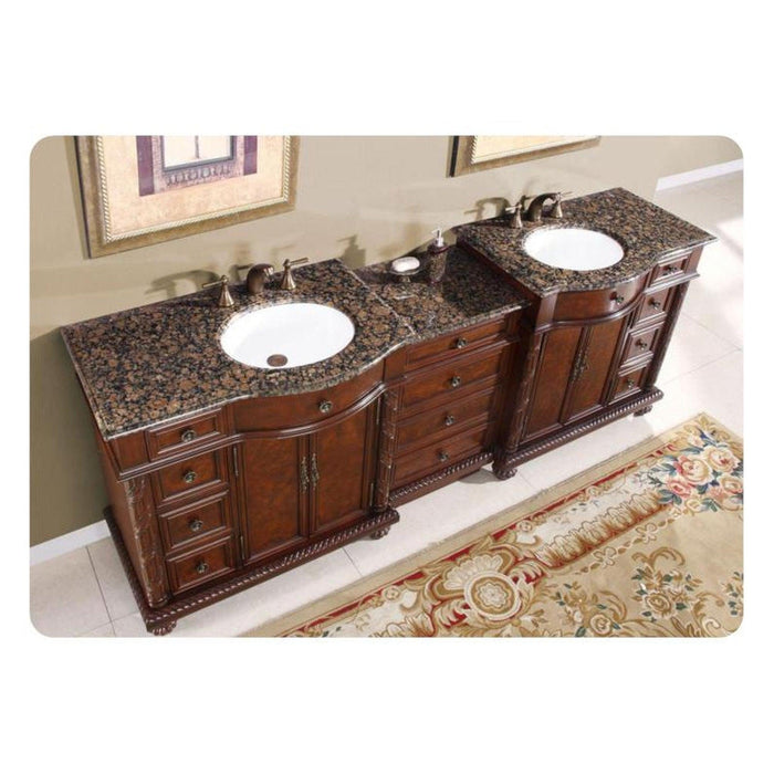 Luxurious wooden bathroom vanity with dark granite countertop, featuring two white sinks and ornate carved details, sitting on an elegant floral area rug.