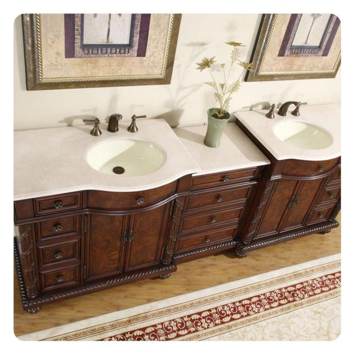 Elegant wooden double bathroom vanity with white marble countertop, two sinks, decorative dark wood cabinetry, and small plant in green vase