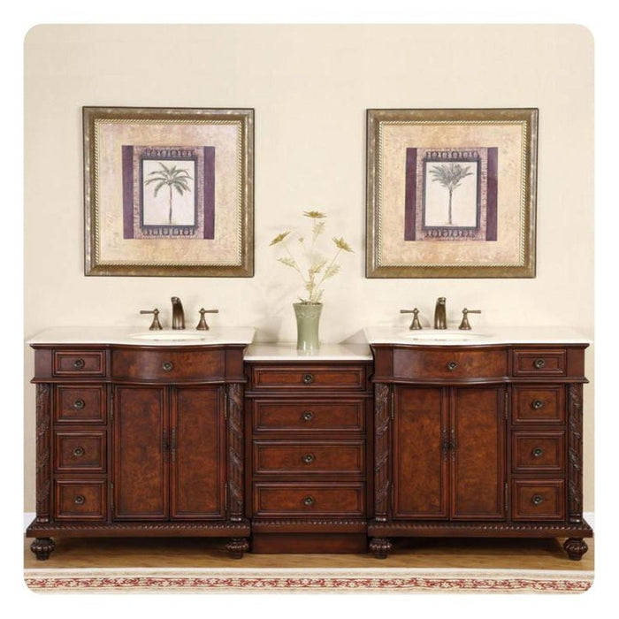 Rich wood double vanity with white sinks, framed palm tree art, and delicate vase between matching sinks on cream wall.