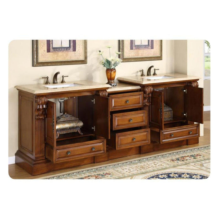 Luxurious wooden bathroom vanity with double sinks, marble countertop, ornate carved details, and multiple drawers, styled with decorative vase and framed artwork.