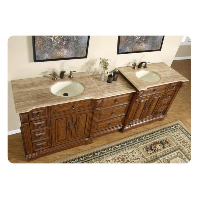 Ornate wooden double bathroom vanity with travertine countertop, two sinks, and decorative rug beneath.