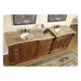 Ornate wooden double bathroom vanity with travertine countertop, two sinks, and decorative rug beneath.
