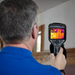 Teledyne FLIR E54 24 person using camera facing wall thermal display visible.