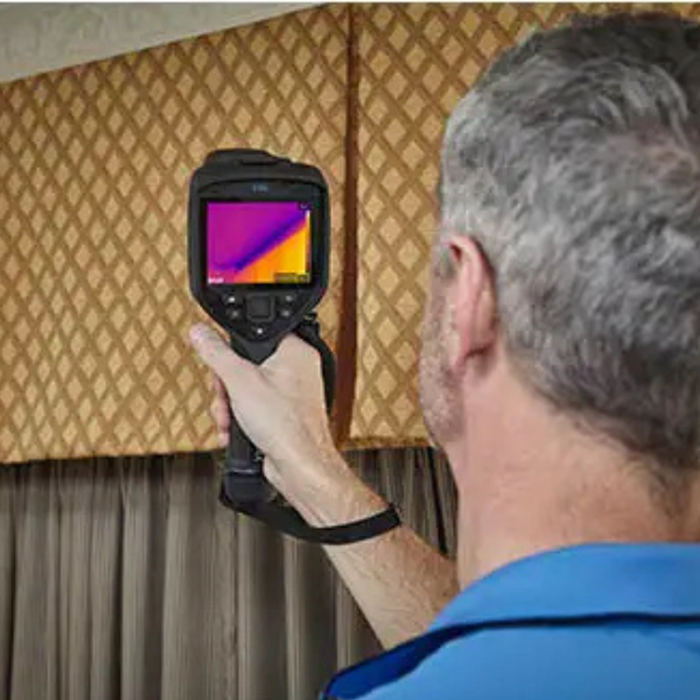 Teledyne FLIR E86 24 14 person holding thermal camera facing window curtains.