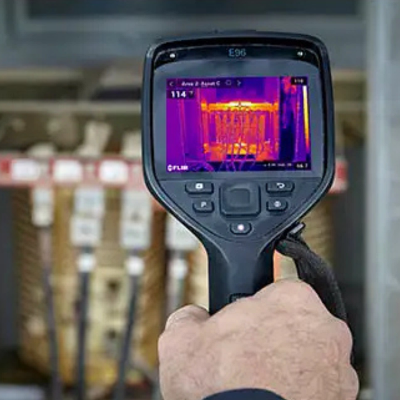 Teledyne FLIR E96 24 42 hand holding camera facing electrical panel with thermal display.