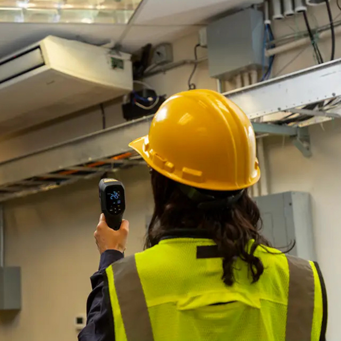 Teledyne FLIR TG54 2 spot thermometer worker in hardhat aiming at ac unit.