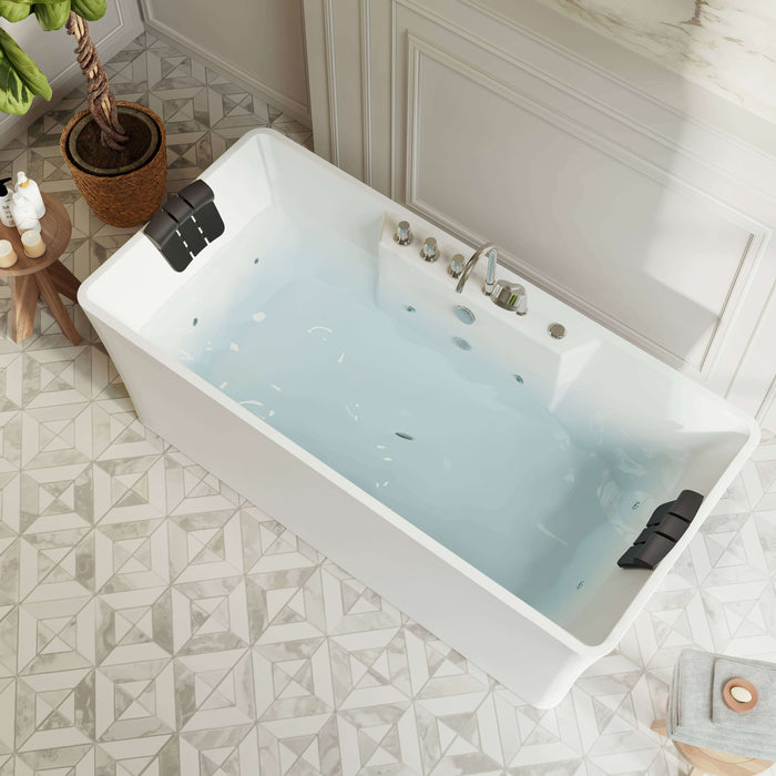 Modern white bathtub filled with blue water, geometric tile floor, potted plant on wooden stool nearby