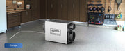 AlorAir Sentinel WHD100 on a garage floor with its drain hose, labeled Garage