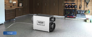 AlorAir Sentinel WHD120 on a garage floor with its drain hose, labeled Garage