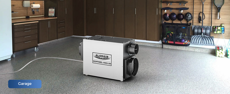 AlorAir Sentinel WHD120 on a garage floor with its drain hose, labeled Garage