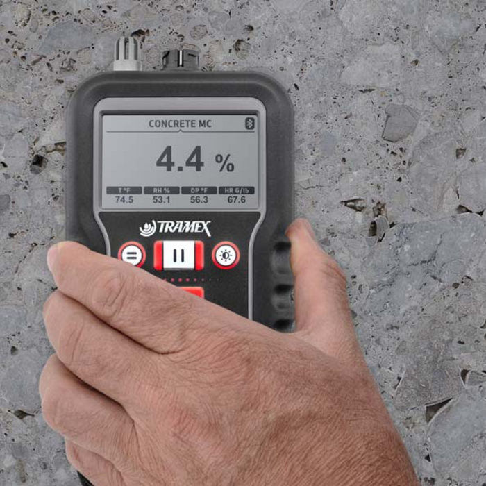 Tramex Flooring Installation Quick Check Plus Kit - IQCPK: Image of the Tramex CMEX 5 moisture meter on a concrete surface, used for measuring moisture levels during flooring installation, with an iPhone displaying the TM app in the background.