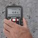 Tramex Flooring Installation Quick Check Plus Kit - IQCPK: Image of the Tramex CMEX 5 moisture meter on a concrete surface, used for measuring moisture levels during flooring installation, with an iPhone displaying the TM app in the background.