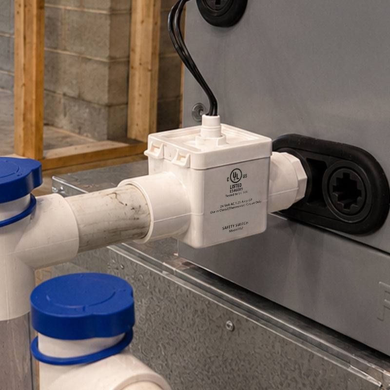 CoolGuard trap kit float switch installed at an air handler drain outlet, with blue drain caps on the tees