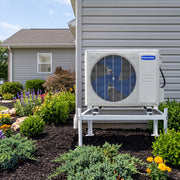 MRCOOL condenser on a CoolGuard Weldbracket stand in a flower bed beside a sided house