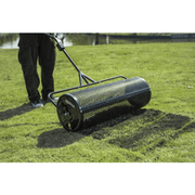 Dapper Supply 36-inch compost spreader laying top dressing on a lawn by a pond.