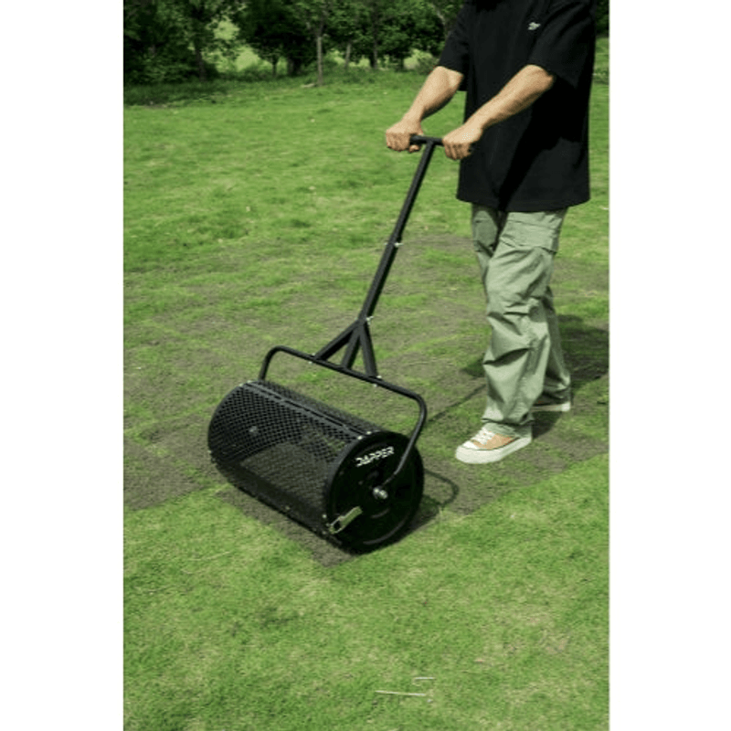 Dapper Supply compost spreader in use spreading material across an open grass field.