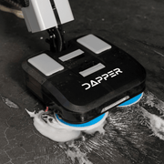 Dapper Supply 16-inch battery walk-behind floor scrubber scrubbing soapy foam from a floor.