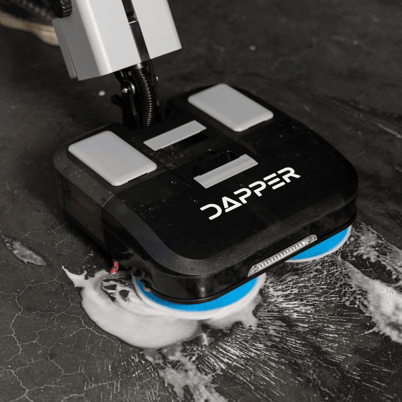 Dapper Supply 16-inch battery walk-behind floor scrubber scrubbing soapy foam from a floor.